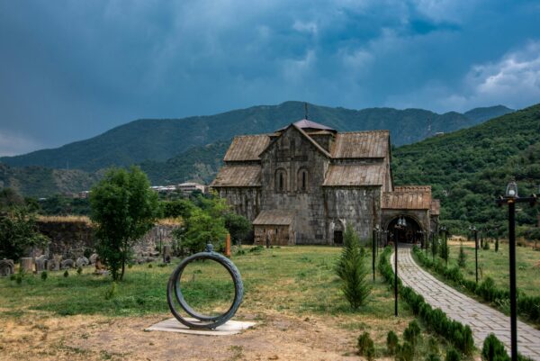 Explore an ancient church set against lush mountains with an adjacent cemetery and a striking sculpture.