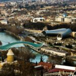 Stunning aerial shot of Tbilisi featuring the Bridge of Peace and modern architecture along the Kura River.